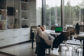 Working overtime in office, tired senior manager satisfied with his work resting in chair after work day..