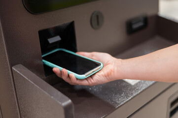 Woman using smartphone online financial transactions at ATM. NFC online banking concept. 