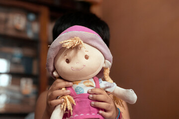Portrait of a little Indian girl obscuring her face while playing with a doll. Selective focus on...