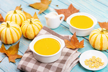 Pumpkin Cream soup served with seeds on blue wooden rustic background. Top view of Autumn cream-soup in country style and fallen autumn maple leaves. Useful dietary snack and lunch