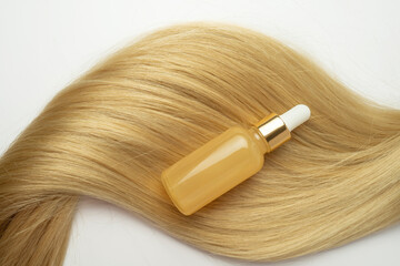 A beauty serum with vitamin C or smoothing oil for hair care lying on the strand of blonde hair