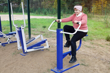 Fototapeta premium Chubby joyful girl performs sports exercises on street simulators