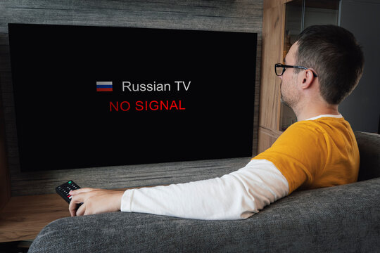 Concept Of Disconnecting Russian Channels In Europe And The USA. Blocking Of Russian TV Broadcasting. Young Handsome Man Watching TV On A Sofa At Home.