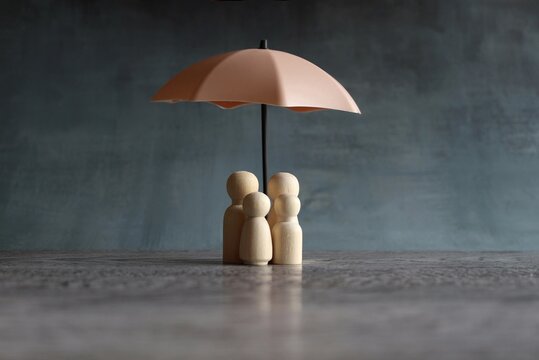 Umbrella and wooden dolls with copy space. Family protection and insurance coverage concept.