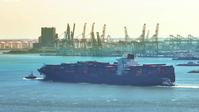 Container ship entering the port of Rotterdam from the North Sea and is sailing towards the container terminal. Aerial view drone footage from above.