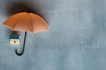 Umbrella and toy house with copy space. House protection and insurance coverage concept.