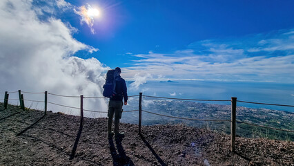 Man with backpack enjoying scenic view from volcano Mount Vesuvius on bay of Naples, Province of Naples, Campania, Italy, Europe, EU. Looking at city of Naples and Mediterranean coastline on sunny day