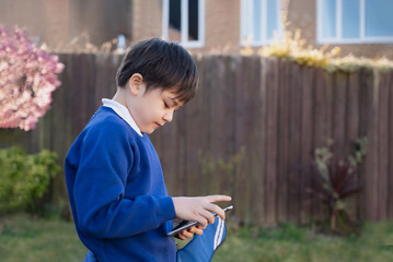 Happy kid holding tablet pc standing outside waiting for School bus, Child boy playing game online...