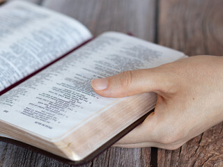 Naklejka premium Female hand holding an open Holy Bible Book with golden pages. A closeup. Reading and studying Scriptures, Christian education, biblical concept.
