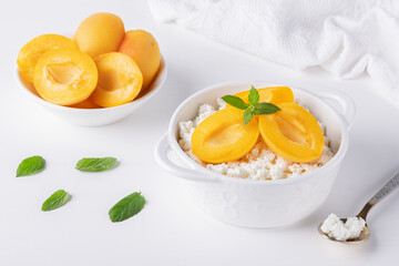 Fresh cottage cheese in white bowl with mint leaves and peach pieces and teaspoon on white...
