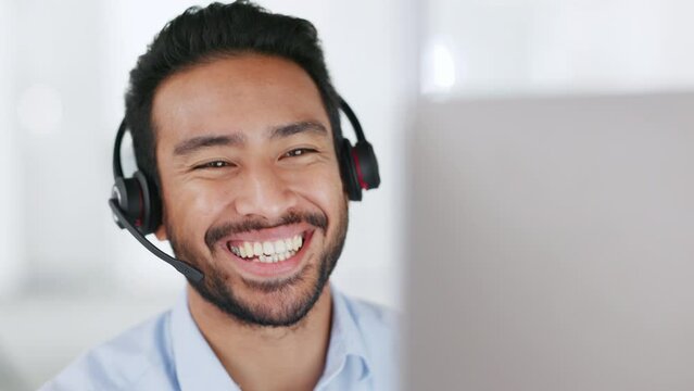 A male call center or telecom agent happy and smiling after providing good customer service. Young business man talking on a video conference call looking at PC wearing headset working from home
