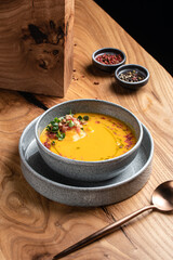 A plate of pumpkin cream soup garnished with microgreens and tomatoes on a wooden table. restaurant food