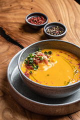 A bowl of pumpkin cream soup garnished with microgreens and tomatoes served in a gray bowl. restaurant food