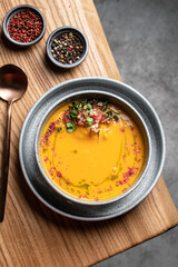 A plate of pumpkin cream soup garnished with microgreens and tomatoes on a wooden table, top view....