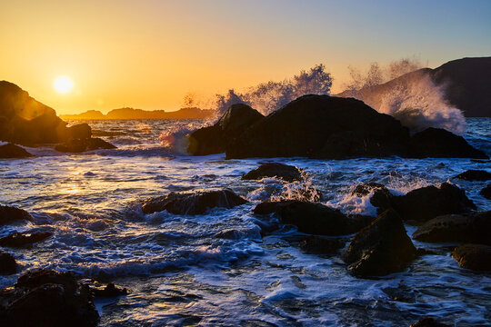 Waves crashing over boulders on ocean during sunset © Nicholas J. Klein