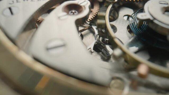 Moving metal gears inside working pocket watch mechanism. Working clock mechanism with rotating spring, gears, gearing and toothed wheels. Inside view of a moving clockwork. Macro shot. Rack focus.