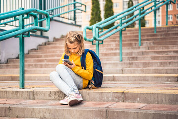 Back to elementary, primary school. Little girl with backpack,mobile phone. Chat, talk with...