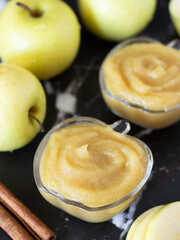 Organic homemade apple puree with a swirl on top in a glass bowl with cinnamon and golden delicious...