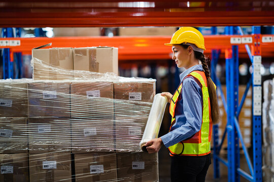 A female worker wrapped a parcel of stretch film on a cargo in a large factory warehouse. Logistics and export industry concept.