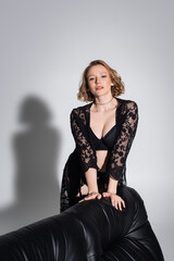 Fototapeta premium seductive woman in black underwear and lace tunic smiling at camera on grey background.