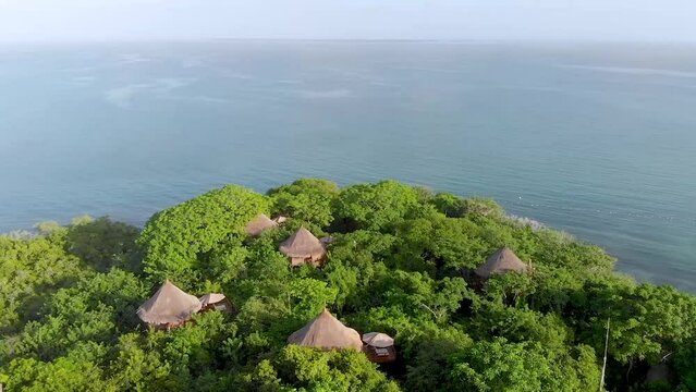 Aerial panoramic view flying over some natural bungalows, tree houses and a tropical beach surrounded by a green forest in Baru, Cartagena, Colombia