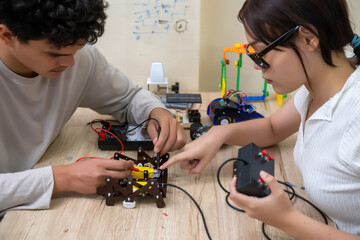 Teenage students build learning with robotic vehicles at desks in STEM engineering science...