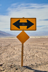 Yellow road sign T intersection left or right in sandy desert