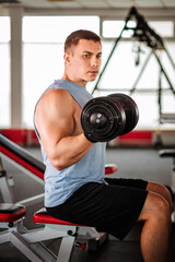 Fototapeta na wymiar Muscular man trains in the gym, doing exercises with dumbbells for biceps, strong male abs