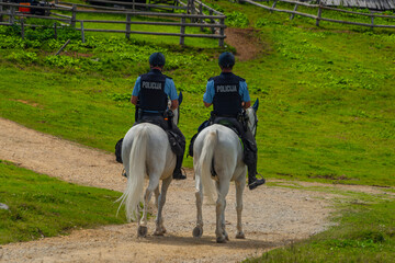 Blue policemans on white horses on path in Velika Planina mountains in holiday