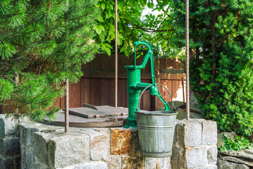 Stone water well with an old metal bucket in green garden