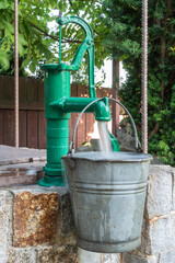 Stone water well with an old metal bucket in green garden