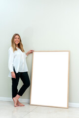 very cheerful young blonde woman in casual clothes holding a large blank poster picture