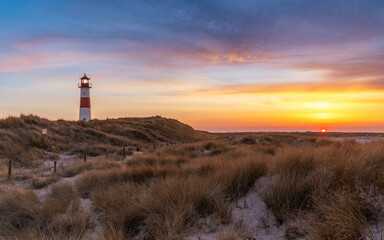 Sonnenuntergang auf Sylt mit dem Leuchtturm List-Ost, romantischem Strand im Vordergrund und einem dramatischen Himmel im Hintergrund