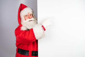 Fototapeta na wymiar Santa Claus peeks out from behind an ad on a white background. Merry Christmas.