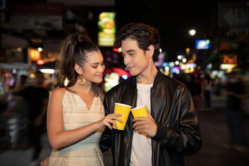 Portrait of happy couple drinking alcohol and having party together. Young man and woman tourist travel in city spend time on holiday vacation together holding bottle of beer at dark night on the road