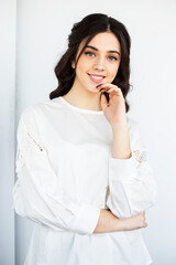 Beauty front portrait of a beautiful smiling young woman wear white shirt, posing in a studio holding hand near face, isolated white background.
