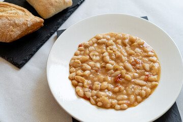 Top view, beans cooked with vegetables, on a white plate, accompanied by rustic bread.