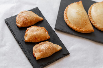 Spanish and Argentininan empanadas on a black slate plate, and white background