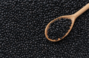 wooden spoon with black beans on a raw black beans background close-up top view.