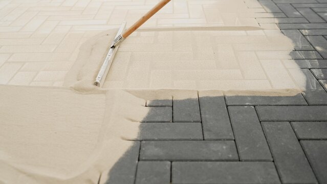 The concept of laying paving stones. A man with sand and a brush closes the seams between the newly installed street tiles on the sidewalk. Seal the seams between the paving slabs. water.