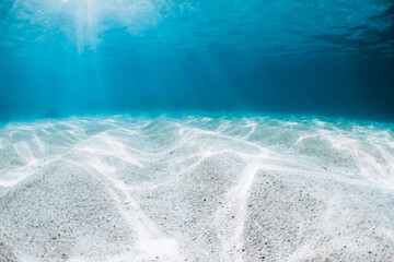 Underwater transparent blue ocean with sandy bottom and sun rays
