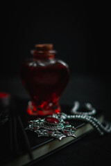 Ritual amulet with red stone, potion, book and wands on a black background.