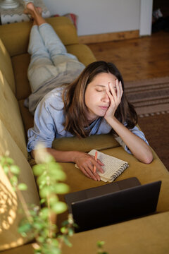 Woman with laptop and notebook lying on the sofa at home