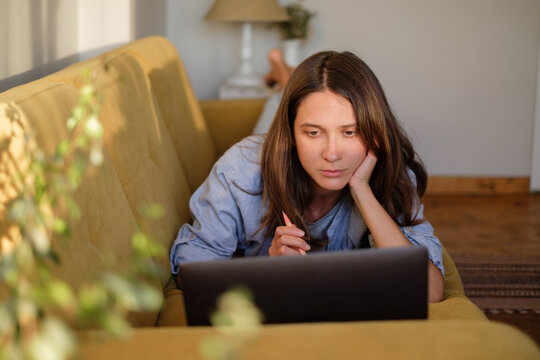 Woman with laptop and notebook lying on the sofa at home