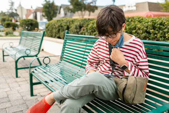 Boy at bench using smartphone at street