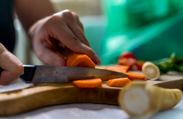 Fototapeta na wymiar A girl is cutting carrot and vegetables on a wooden cutting board during the day
