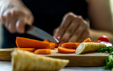 A girl is cutting carrot and vegetables on a wooden cutting board during the day