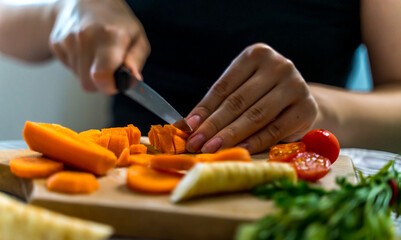 A girl is cutting carrot and vegetables on a wooden cutting board during the day