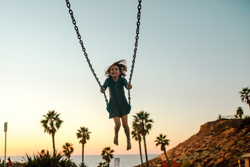 Happy girl on swing at sunset