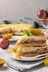 Homemade shortbread plum pie with cut pieces on plate on light gray background